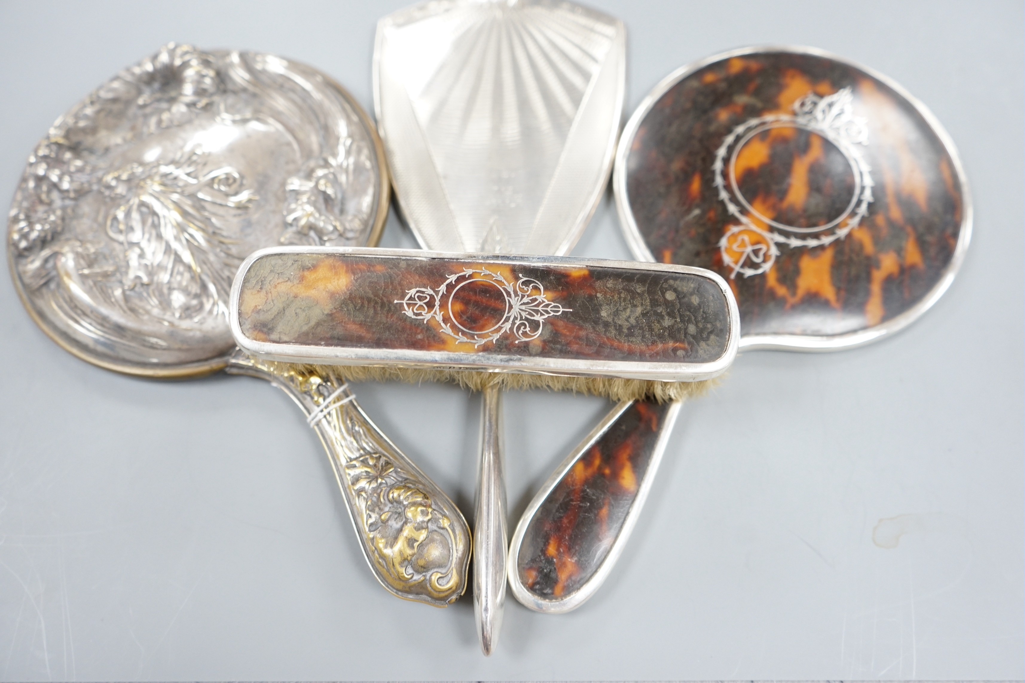 A George V silver and tortoiseshell mounted hand mirror and clothes brush, one other silver mounted hand mirror and a plated hand mirror.